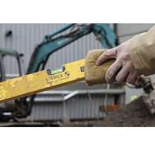 Stabila Wasserwaage Typ 70 wird mit einem Schwamm gereinigt, Hand hält die verschmutzte gelbe Wasserwaage auf einer Baustelle.