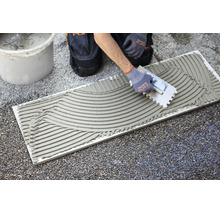 Auftragen von Fliesenkleber auf eine Fliese mit einer Zahnkelle auf einer Baustelle.