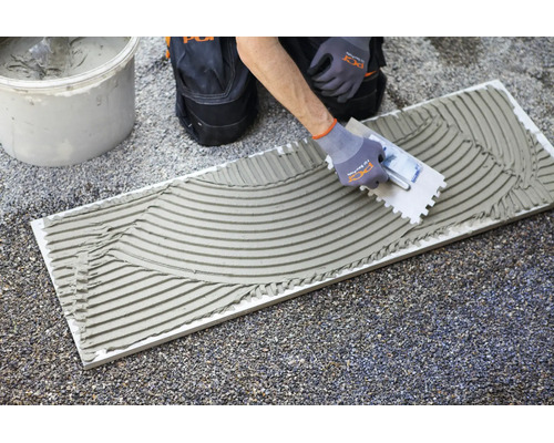 Auftragen von Fliesenkleber auf eine Fliese mit einer Zahnkelle auf einer Baustelle.