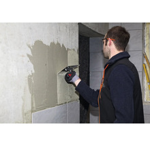 Handwerker beim Auftragen von Fliesenkleber mit einer Zahnkelle an einer Wand für die anschließende Verlegung von Fliesen.
