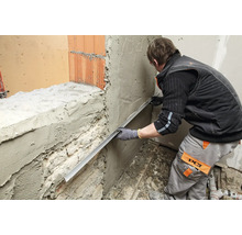 Handwerker zieht mit einer Abziehlatte Putz auf einer Mauer glatt.
