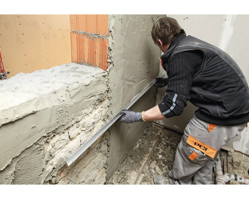 Handwerker zieht mit einer Abziehlatte Putz auf einer Mauer glatt.