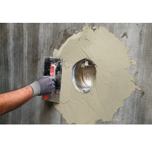 Handwerker beim Verspachteln einer Wandöffnung um eine Unterputz Wanddurchführung mit einer Glättekelle