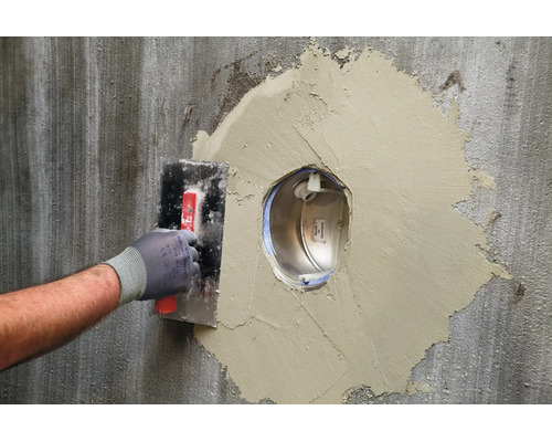 Handwerker beim Verspachteln einer Wandöffnung um eine Unterputz Wanddurchführung mit einer Glättekelle