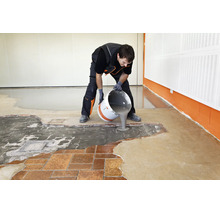 Handwerker gießt Ausgleichsmasse aus einem Eimer auf einen Boden, um ihn für die Verlegung eines neuen Bodenbelags vorzubereiten.