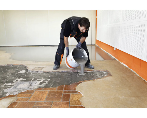 Handwerker gießt Ausgleichsmasse aus einem Eimer auf einen Boden, um ihn für die Verlegung eines neuen Bodenbelags vorzubereiten.