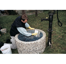 Handwerker beim Verfugen eines runden Gartenbrunnens mit Mosaikfliesen im Außenbereich.