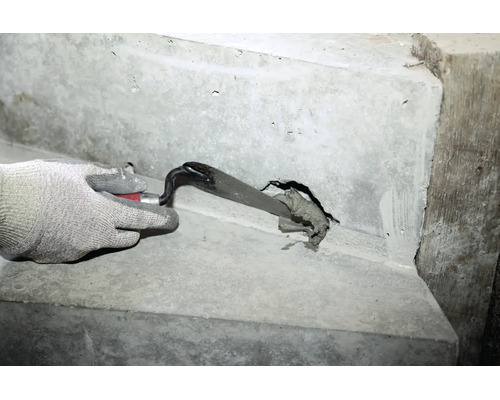 Hand in Arbeitshandschuh spachtelt Mörtel mit einer Maurerkelle in ein Loch in einer Betonwand.