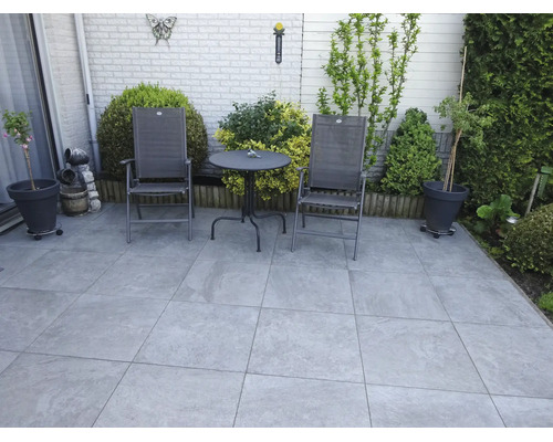 Eine Terrasse mit grossformatigen quadratischen Bodenplatten und einer Sitzgruppe bestehend aus zwei Stühlen und einem runden Gartentisch.