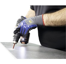Eine Person bohrt mit einer Bohrmaschine ein Loch in eine Fliese und trägt dabei Arbeitshandschuhe.