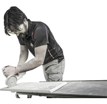 Ein Mann schleift eine Fliese mit einem Winkelschleifer auf einem Tisch.