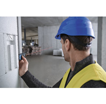 Ein Mann mit Schutzhelm verwendet einen Laser-Entfernungsmesser auf einer Baustelle zur Messung.