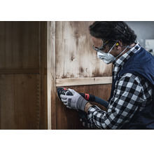 Handwerker schleift Holzschrank mit einem Schleifgerät