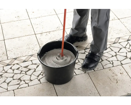 Eine Person mischt Fliesenkleber mit einem Rührwerk in einem Eimer.
