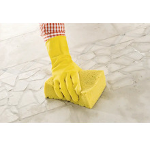 Person mit Gummihandschuh und Schwamm reinigt Fliesenboden.