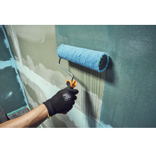 Hand mit Arbeitshandschuh streicht eine Wand mit einer Farbwalze