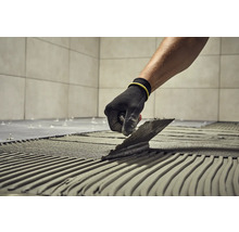 Fliesenleger trägt mit einer Kelle Klebstoff auf einen Untergrund auf