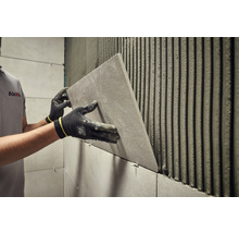 Fliesenleger bei der Arbeit mit einer Fliese an einer Wand mit Fliesenkleber