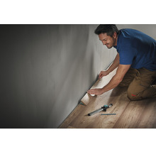 Mann verlegt Laminat mit Werkzeug entlang einer Wand