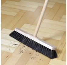 Kehrbesen mit Holzstiel auf Holzboden kehrt Schmutz zusammen
