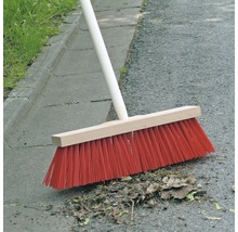 Kehrbesen mit Holzstiel und roten Borsten kehrt Blätter auf Asphalt
