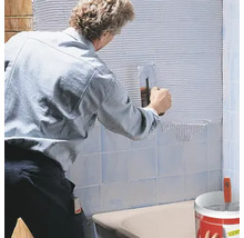 Fliesenleger bei der Arbeit: Anbringen von Fliesen an der Wand mit einem Spachtel