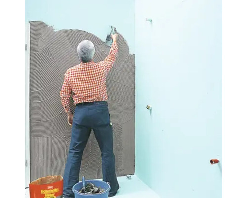 Mann trägt Fliesenkleber auf eine Wand im Badezimmer auf