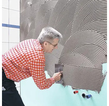 Ein Mann trägt Fliesenkleber mit einer Glättkelle auf eine Wand auf.