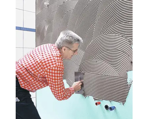 Ein Mann trägt Fliesenkleber mit einer Glättkelle auf eine Wand auf.