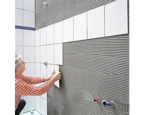 Mann verlegt Fliesen im Badezimmer.