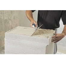 Ein Mann verarbeitet Porenbetonsteine mit einer Mauerkelle.