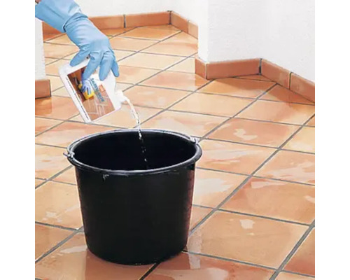 Eine Person mit Handschuhen gießt Reiniger in einen Eimer auf einem gefliesten Boden.