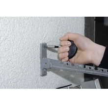 Eine Person befestigt mit einem Schraubendreher einen Metall-Wäscheständer an einer Wand.