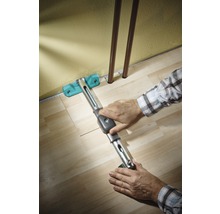 Person verlegt Laminat mit einem Zugeisen entlang einer Wand.