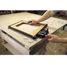 Holzrahmen wird mit einer Rahmenzwinge auf einer Werkbank fixiert.