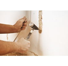 Ein Handwerker stemmt mit Hammer und Meißel eine Nut in eine Wand.