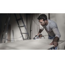 Mann schneidet Holzplatte mit Handkreissäge in Werkstatt