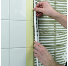 Ein Mann bringt eine Fliesenschiene an einer Wand mit Fliesen an.