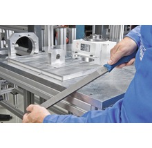 Eine Werkstatt-Szene zeigt eine Hand, die eine Werkstattfeile an einem Metallwerkstück verwendet.