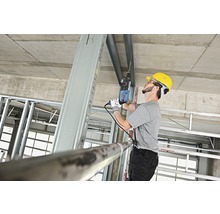 Handwerker bohrt mit einer Bohrmaschine in ein Metallprofil auf einer Baustelle.