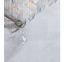 Meißel bearbeitet eine graue Wand und es entstehen Steinsplitter.