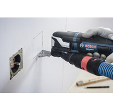 Ein Mann verwendet ein Multifunktionswerkzeug von Bosch, um eine quadratische Öffnung in eine Wand neben einer Steckdose zu schneiden.