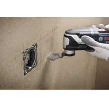 Eine Person schneidet mit einem Multifunktionswerkzeug eine Öffnung für eine Steckdose in eine Wand.