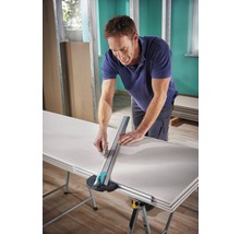 Ein Mann schneidet eine Gipskartonplatte mit einem Gipskartonschneider auf einem Tisch.