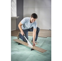 Mann schneidet Laminat mit Laminatschneider auf Trittschalldämmung