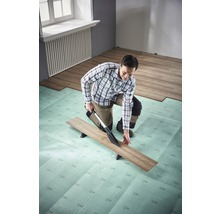 Mann schneidet Laminat mit Laminatschneider auf Dämmunterlage im Raum