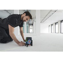 Ein Mann benutzt einen Kreuzlinienlaser von Bosch auf einem Baugelände, um eine Linie auf den Boden zu zeichnen.