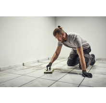 Fliesenleger reinigt Bodenfliesen mit Schwammbrett