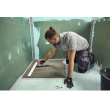 Handwerker, der mit einer Glättkelle Estrich in einem Badezimmer verteilt