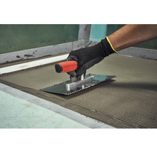 Fliesenleger mit Glättkelle zum Auftragen von Fliesenkleber